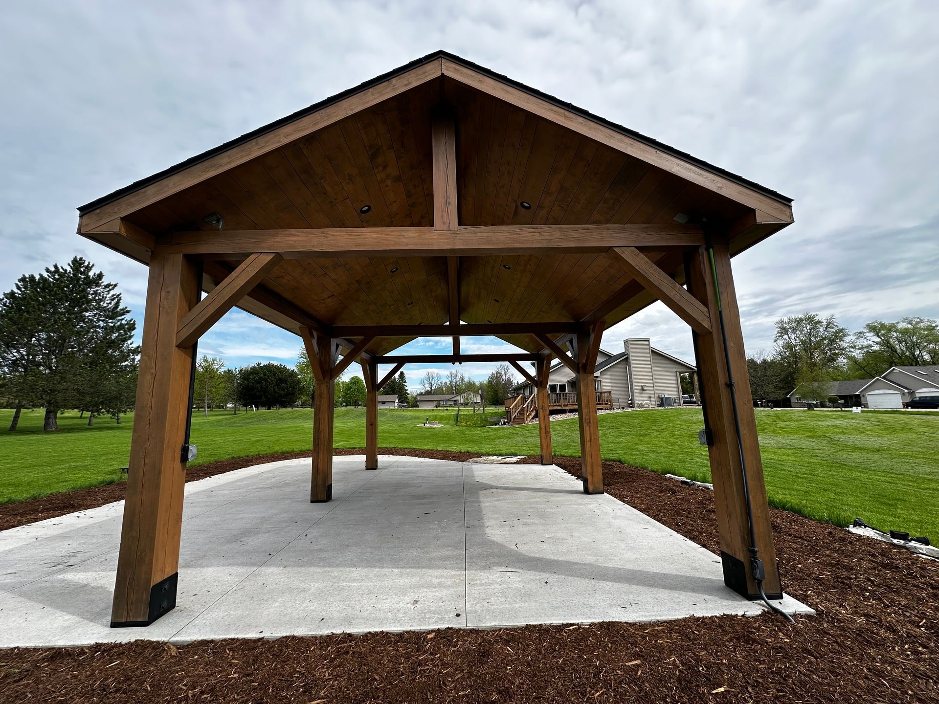 A wooden pavilion is sitting in the middle of a grassy field.