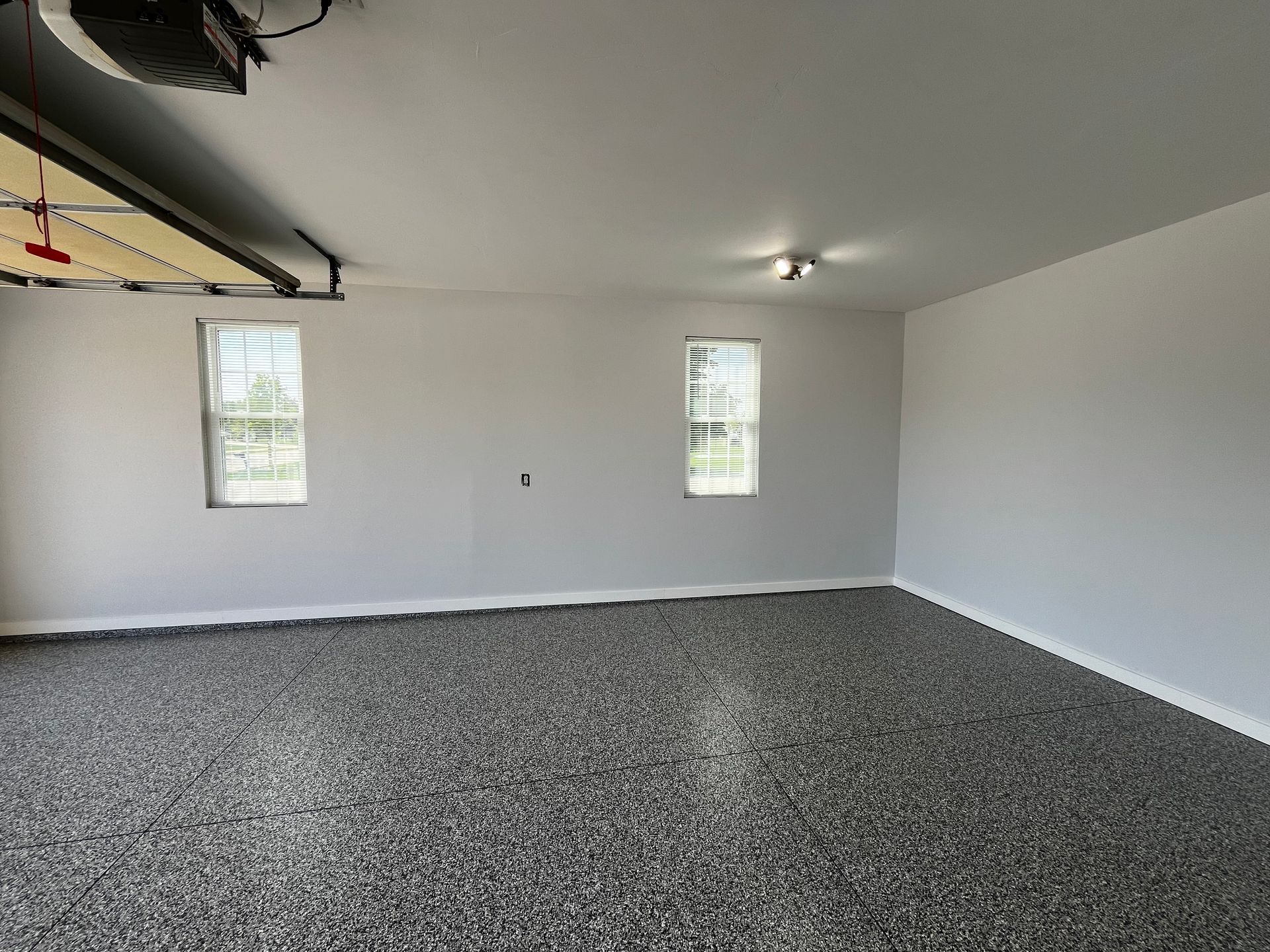 An empty garage with a garage door open and two windows.