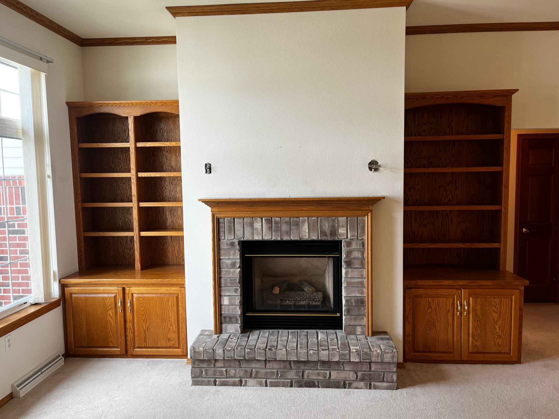 An empty living room with a fireplace and shelves