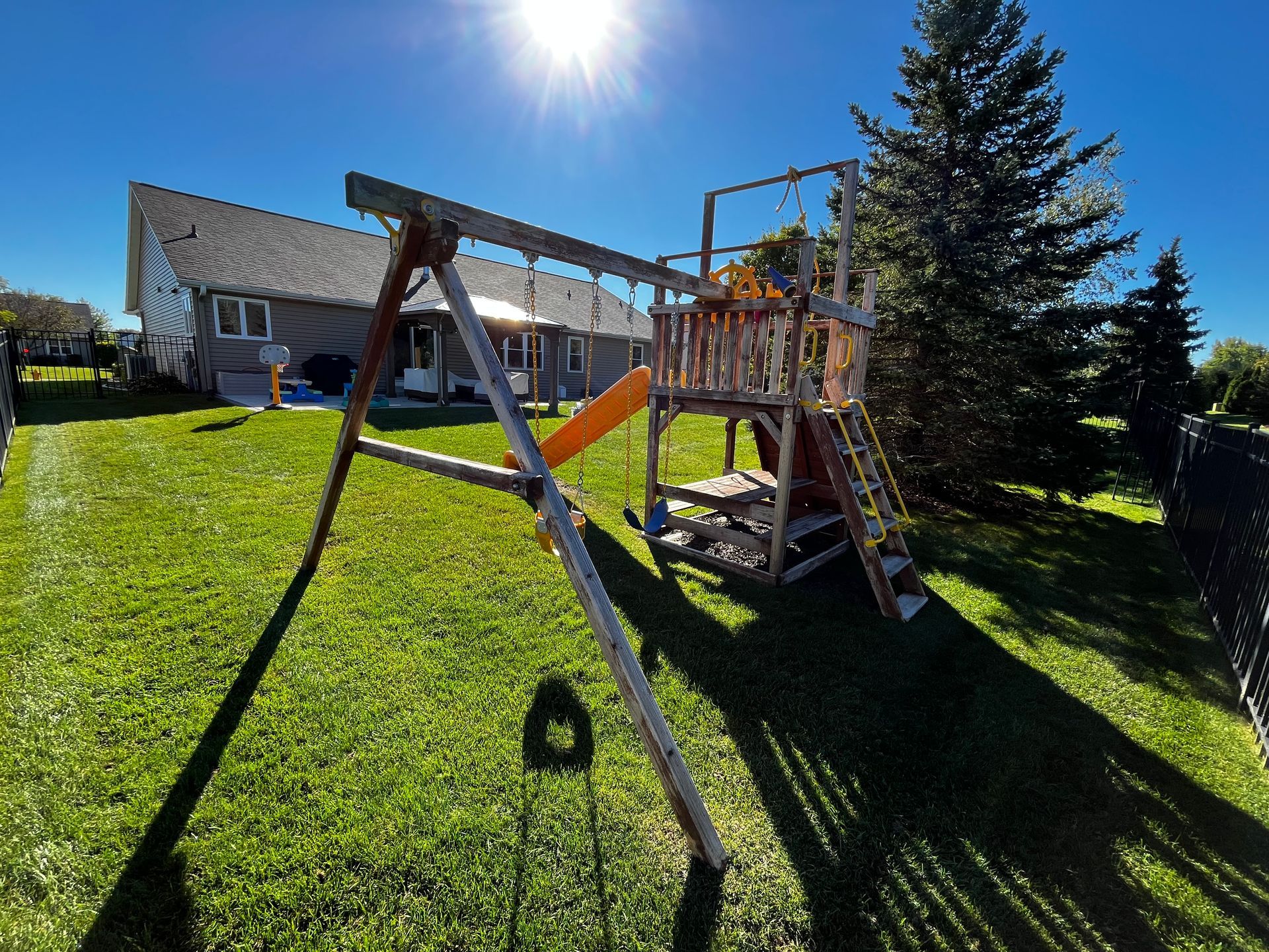 A backyard with a swing set and slide in front of a house.