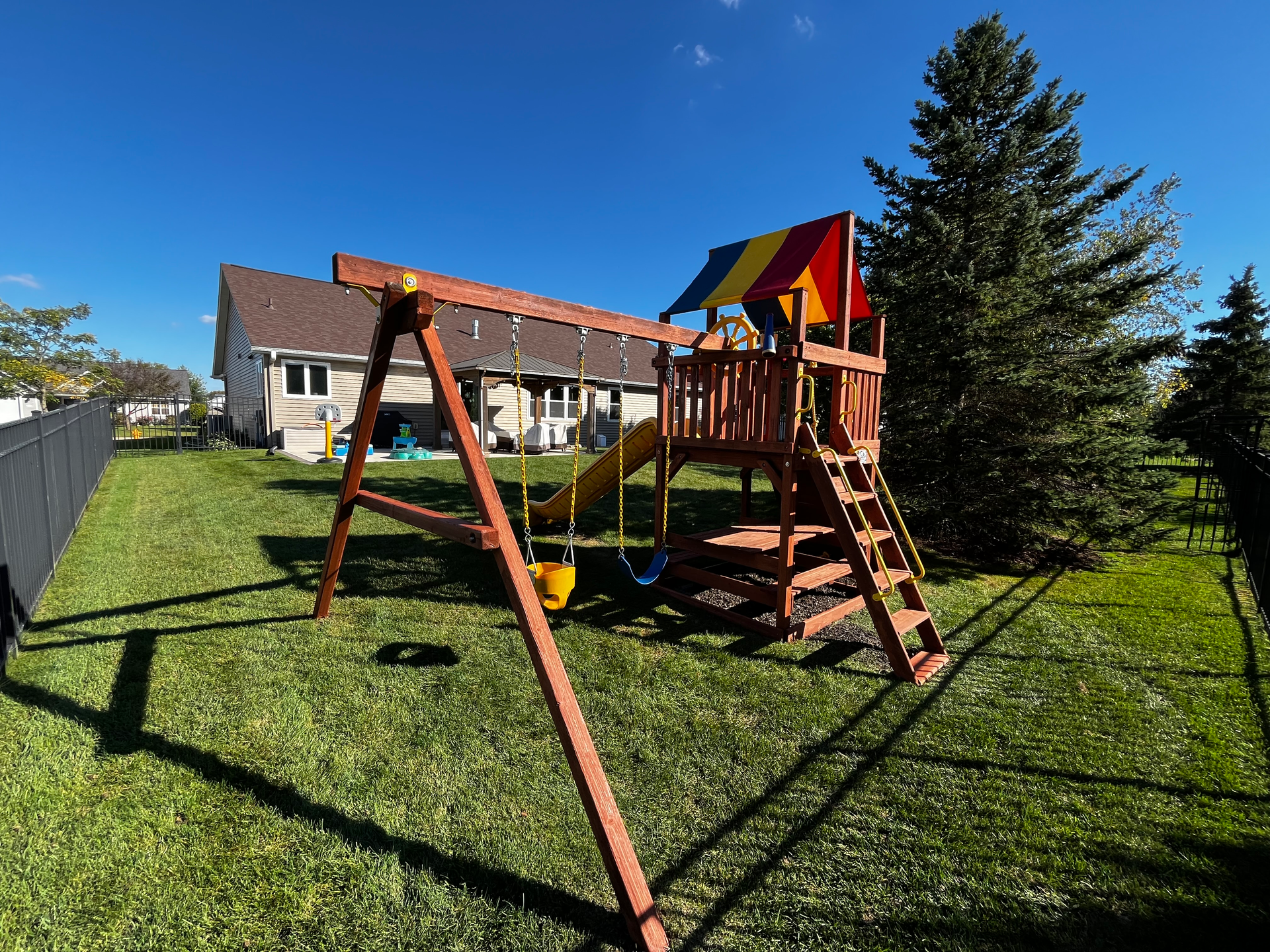 A wooden playground set in the backyard of a house.
