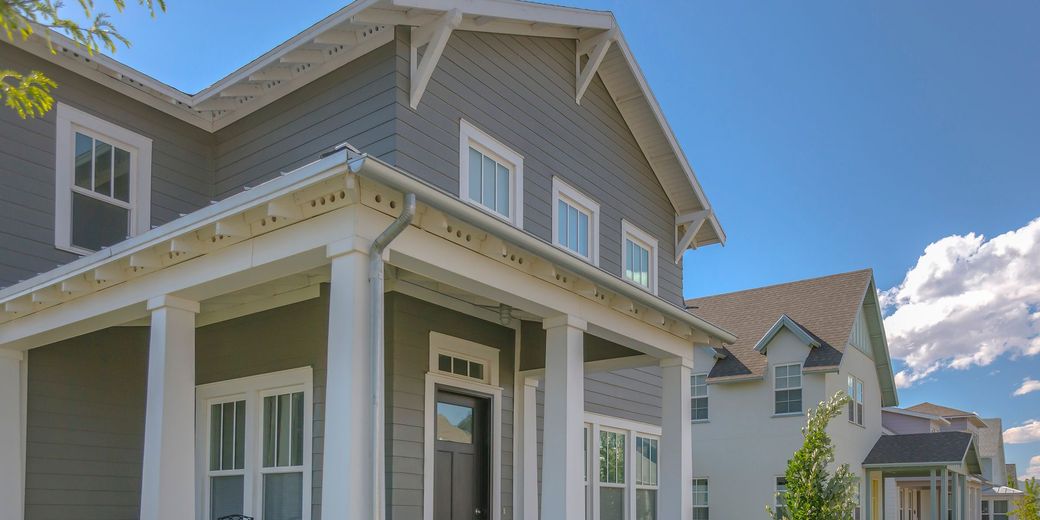 Gray house with white trim and pillars, blue sky.
