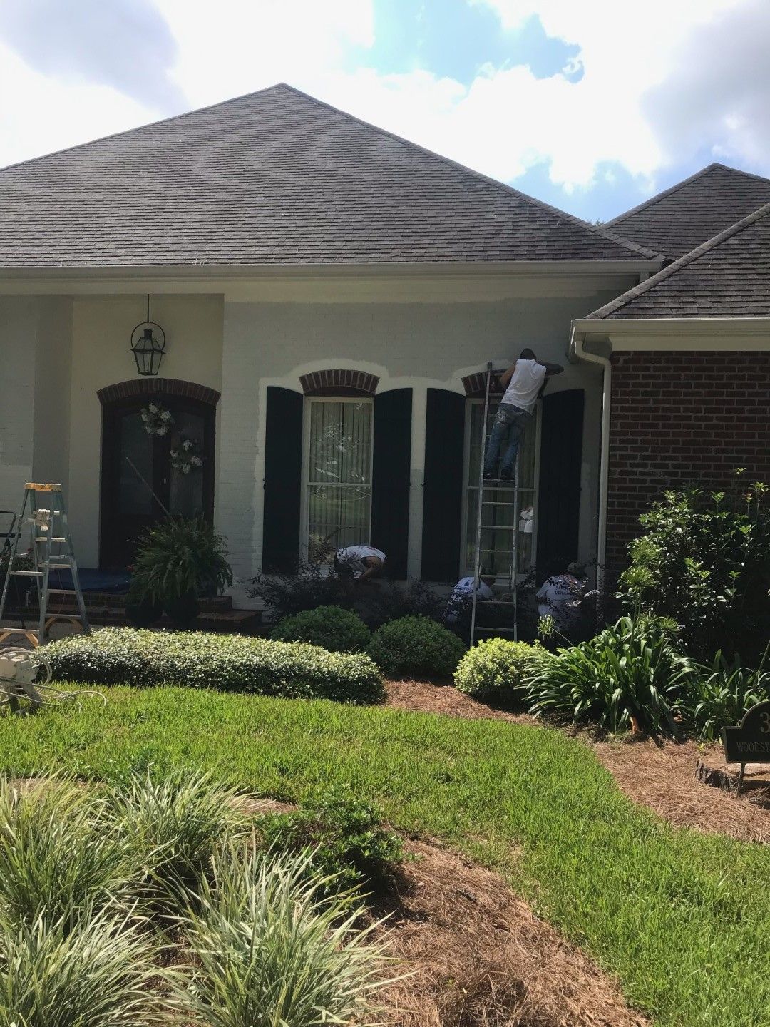 A man is standing on a ladder painting the front of a house.
