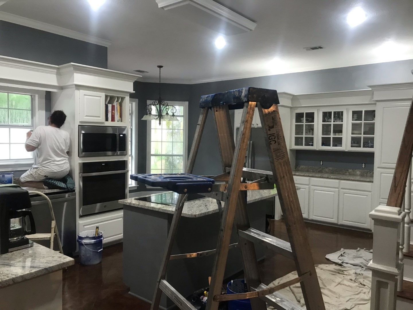 A man is painting a kitchen with a ladder in the foreground.