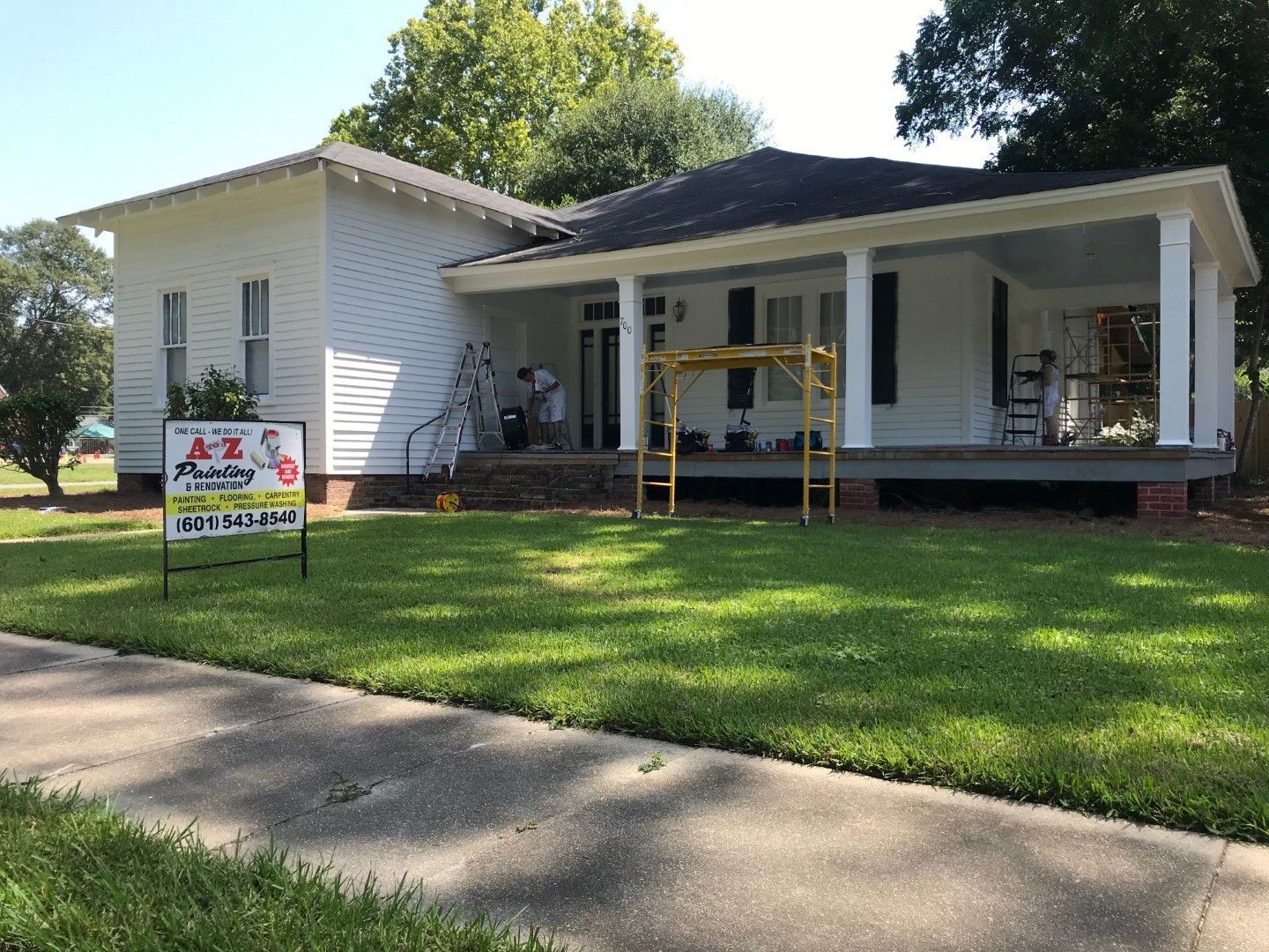 A white house with a porch and a sign in front of it.