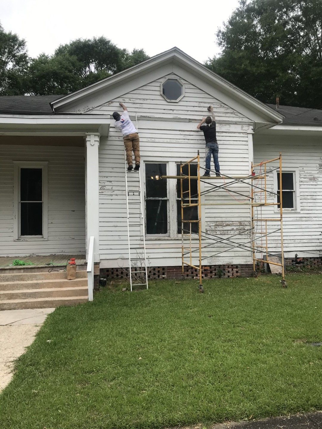 Two men are painting the side of a white house.