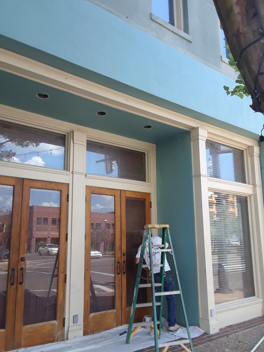 A man on a ladder paints the outside of a building