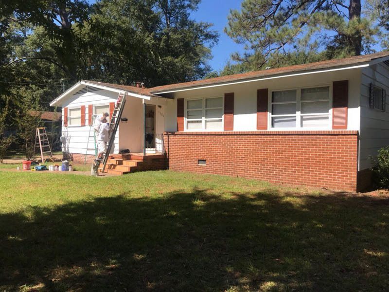 A man is painting the side of a house with a ladder.