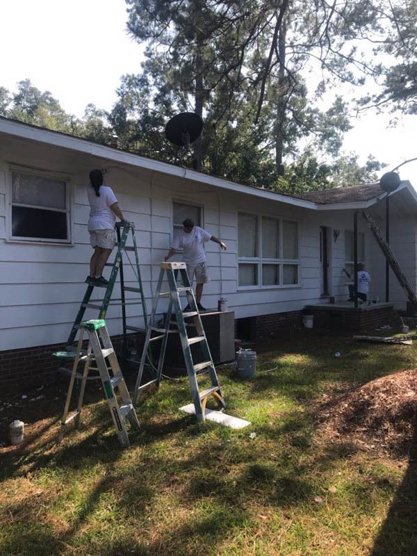 Two people are painting a white house with ladders.