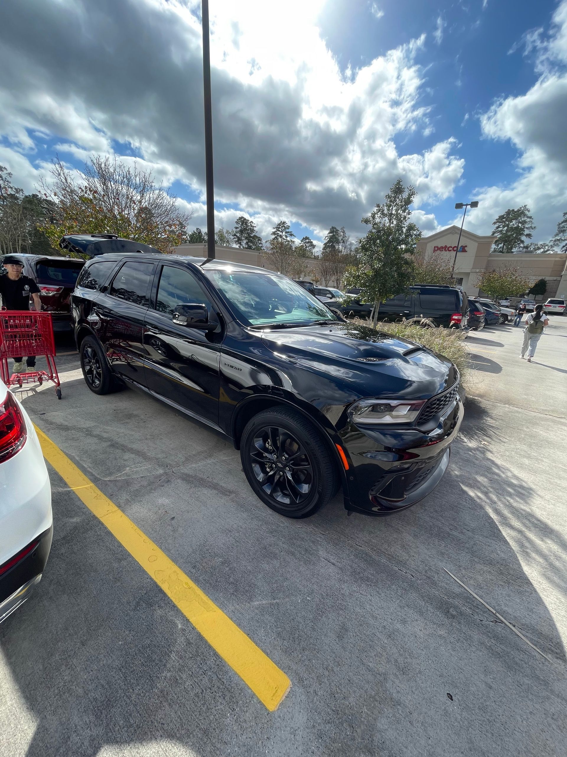 A black car is parked in a parking lot next to a shopping cart.
