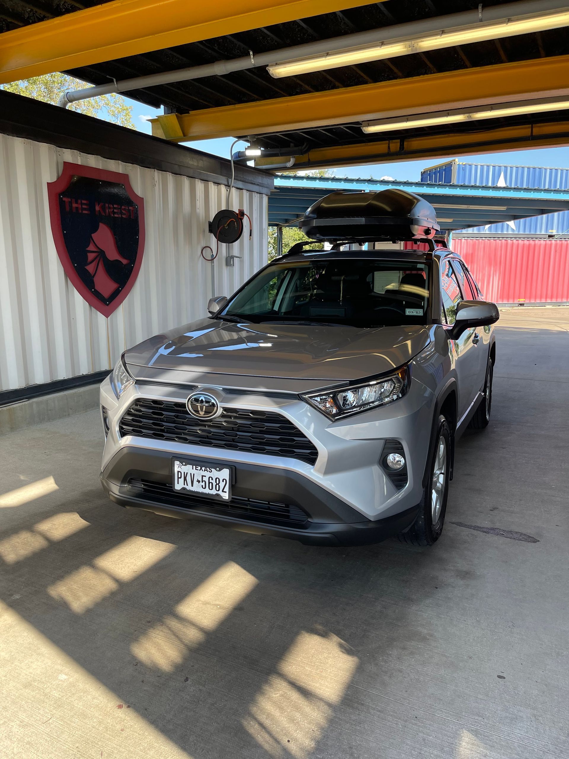 A silver toyota rav4 with a roof rack is parked in a car wash.