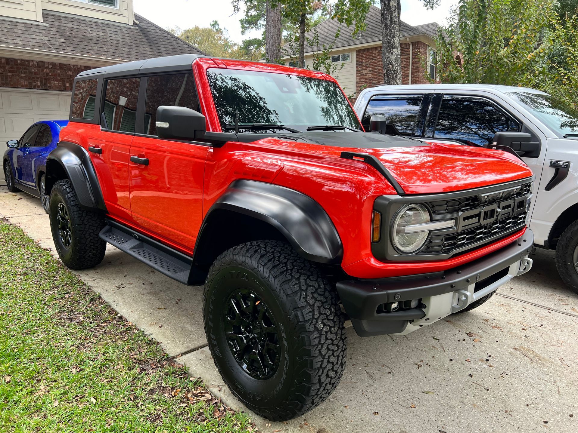 A red ford bronco raptor is parked next to a white ford f150 raptor.