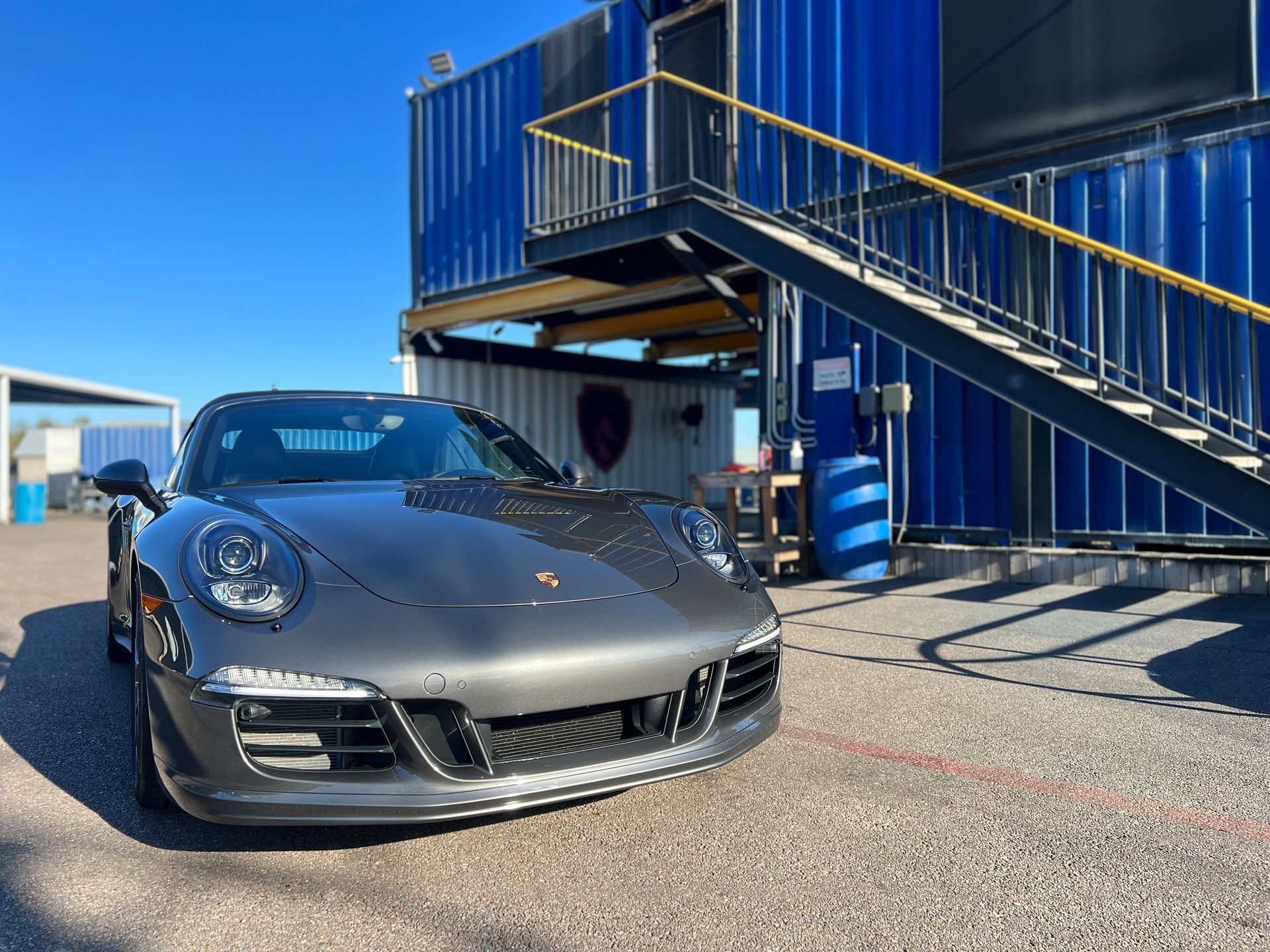 A gray porsche 911 is parked in front of a blue building.