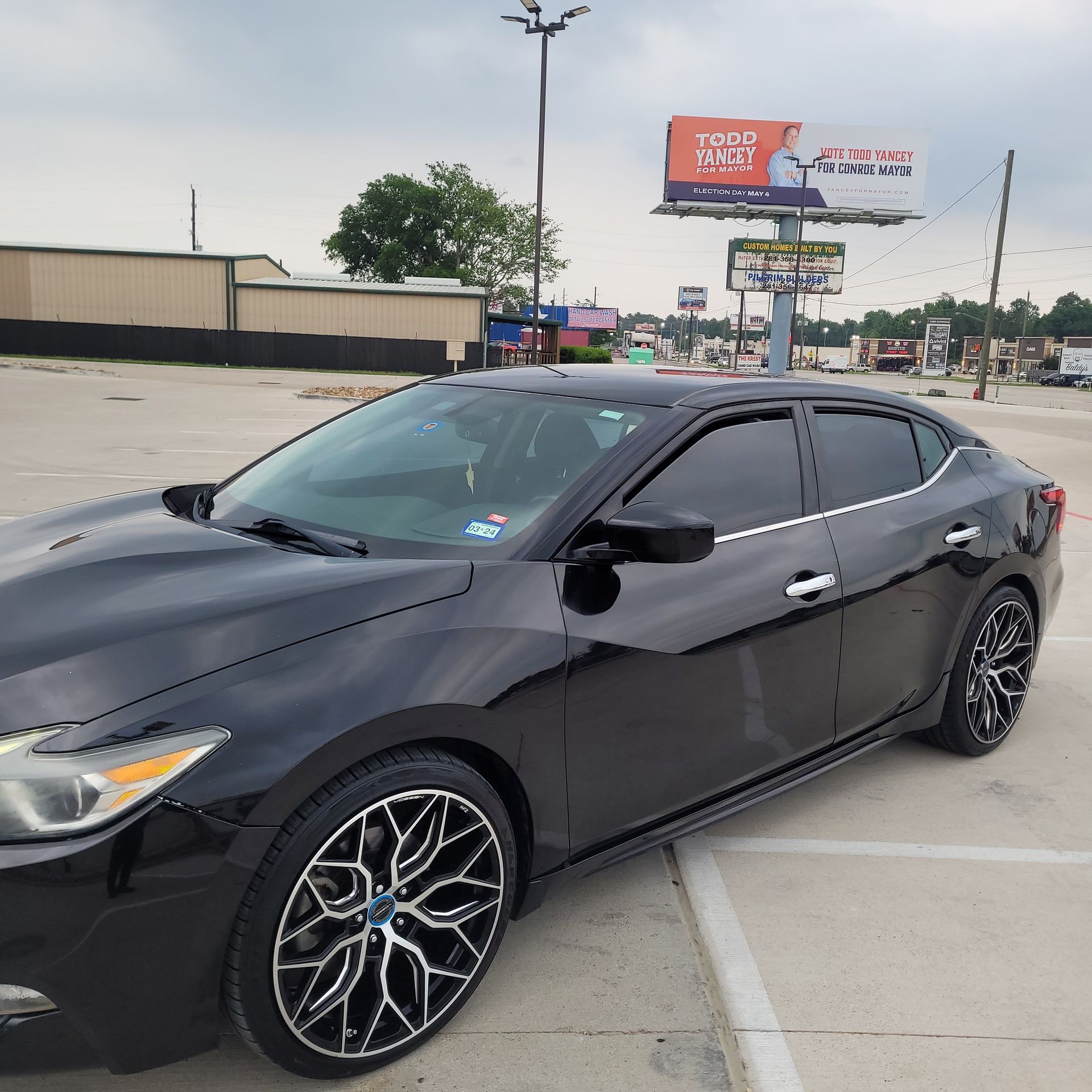 A black car is parked in a parking lot under a billboard that says taco bell