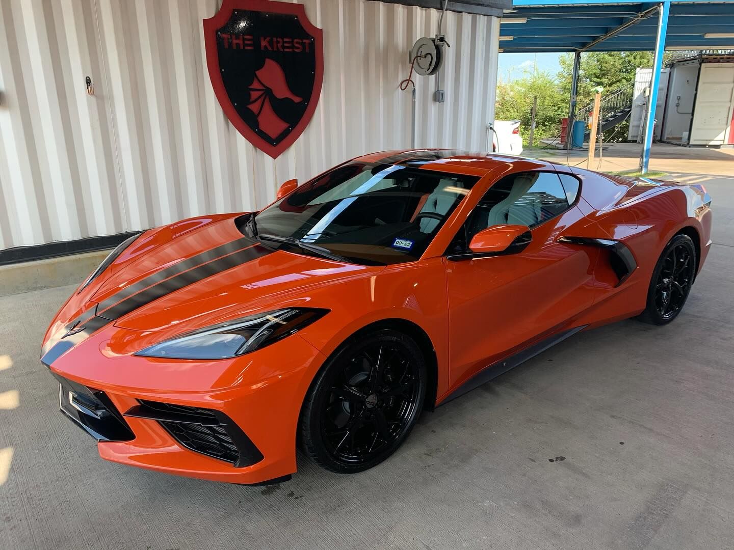 An orange sports car is parked in front of a white building.