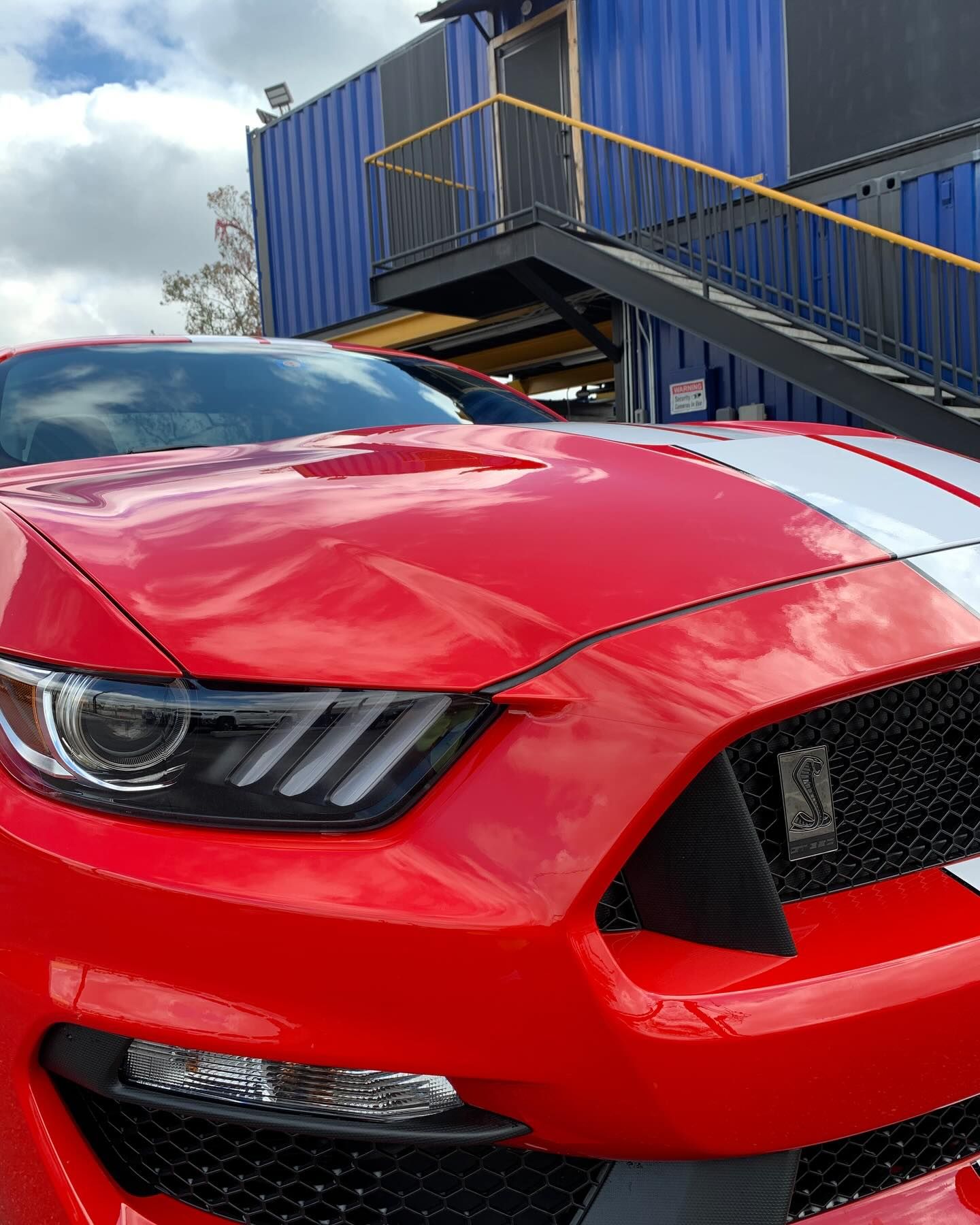 A red mustang is parked in front of a blue building.