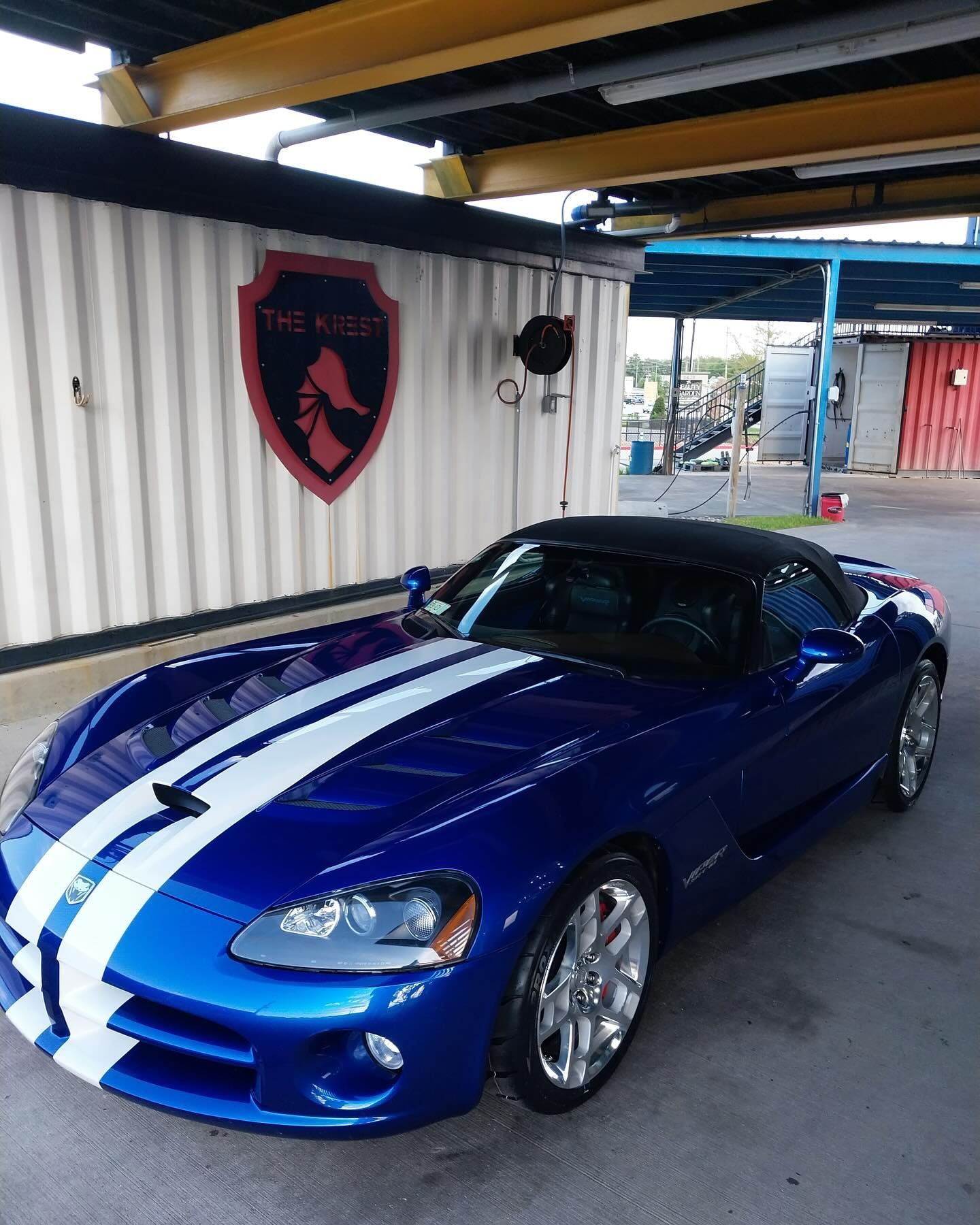 A blue sports car with white stripes is parked in a parking lot