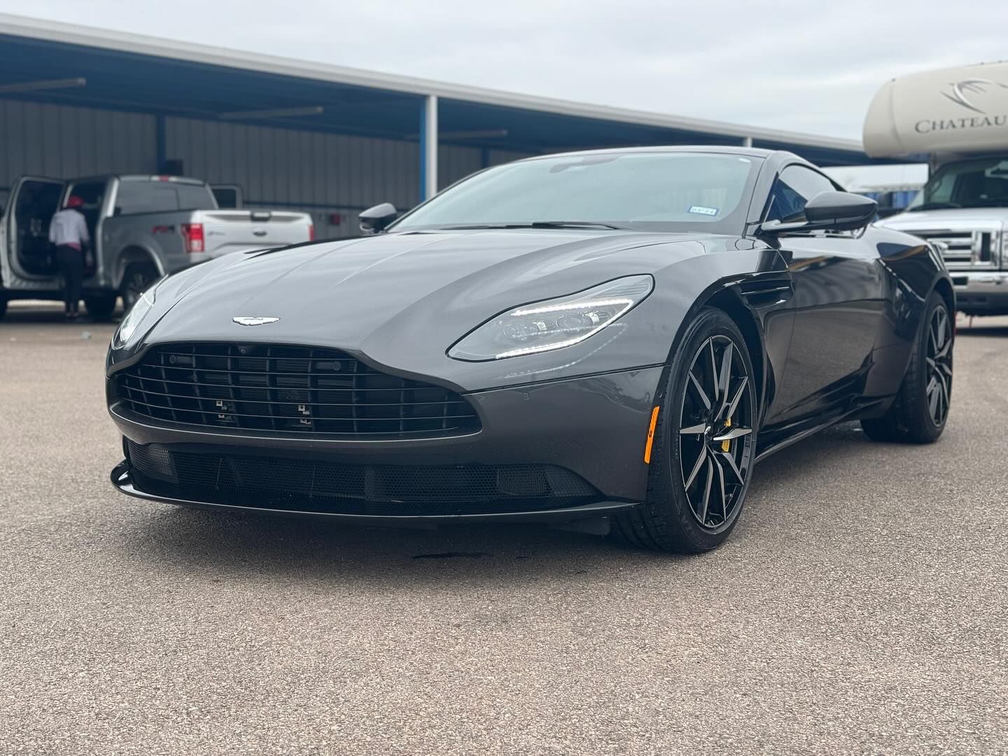 A gray aston martin db11 is parked in a parking lot.