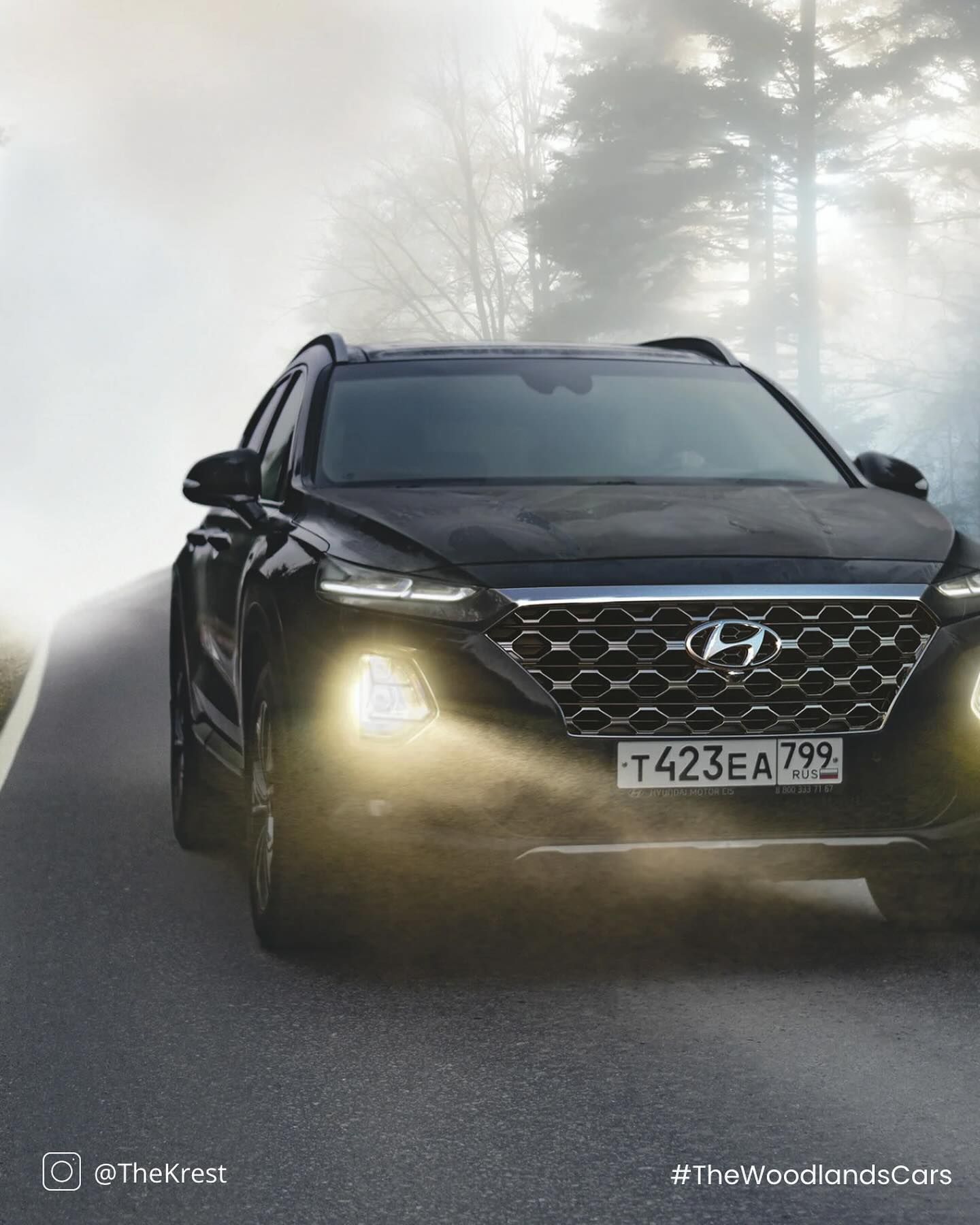 A black hyundai santa fe is driving down a foggy road.