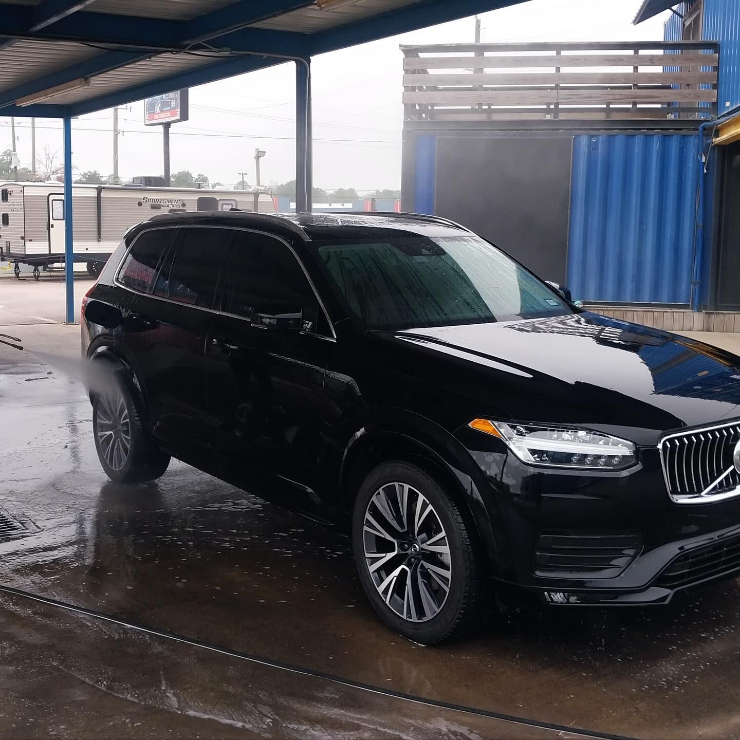 A black volvo is parked under a canopy in the rain