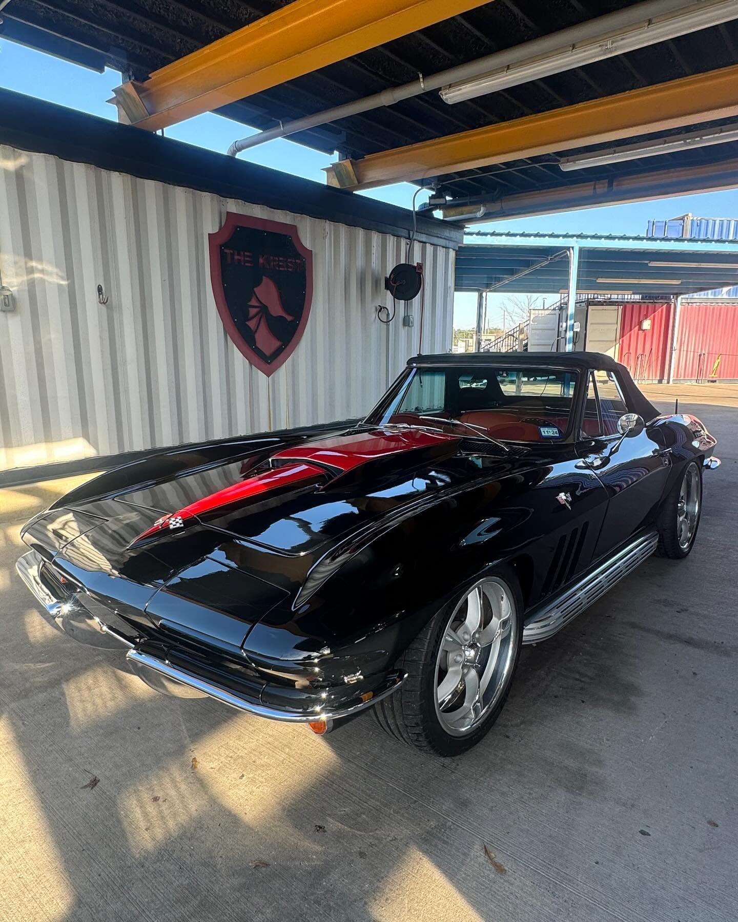 A black and red corvette is parked in front of a building.