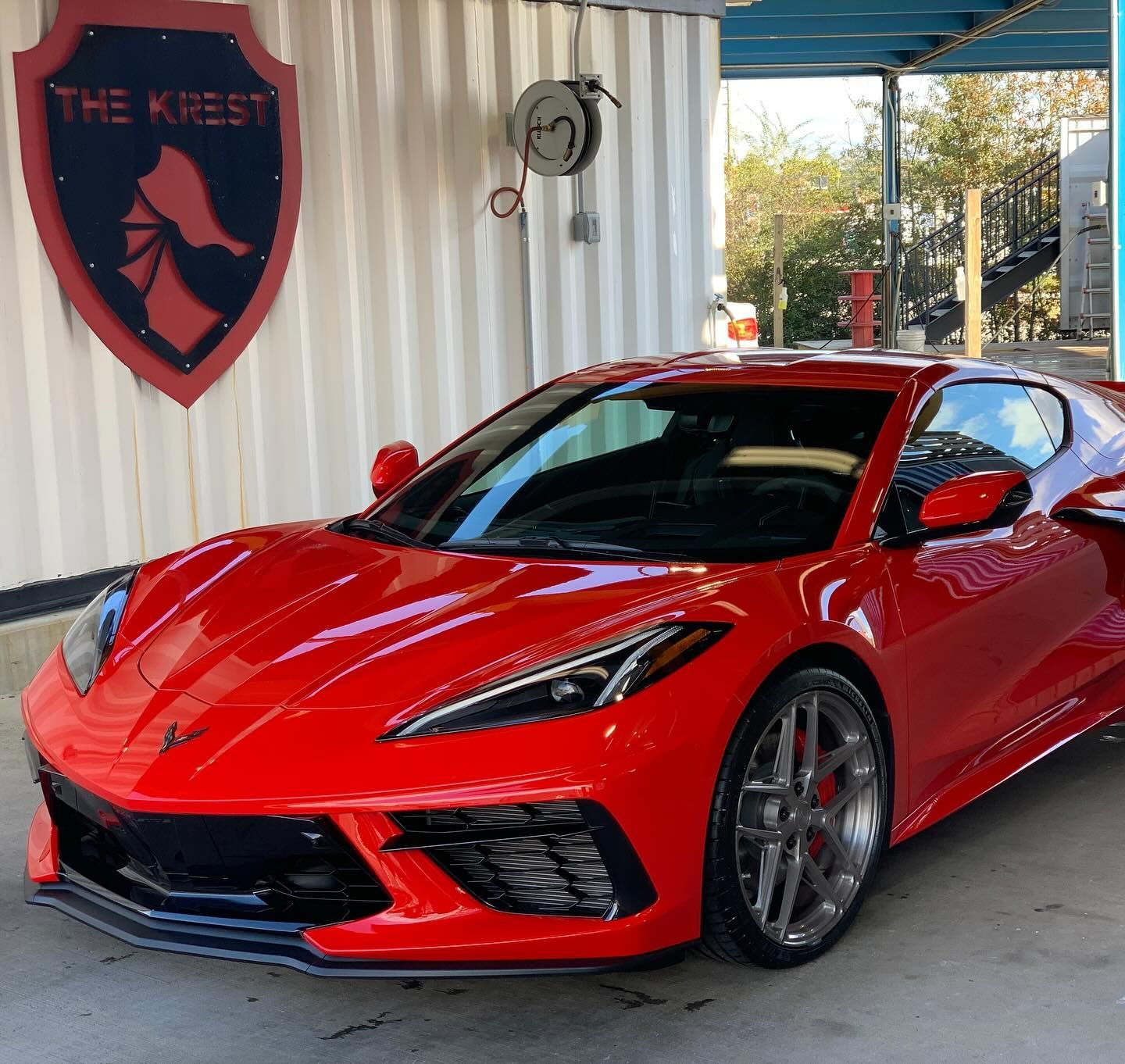 A red sports car is parked in front of a building that says the krest
