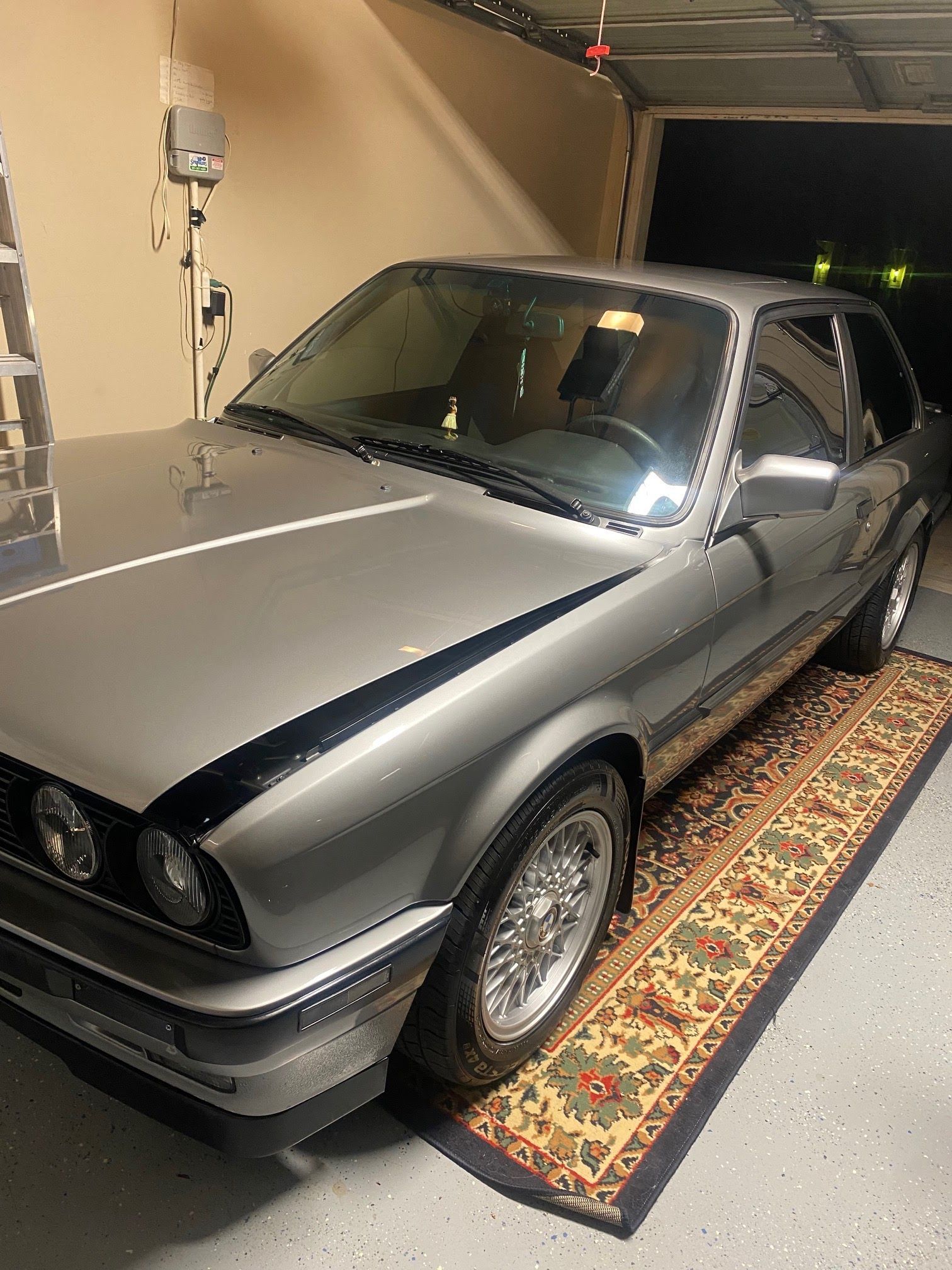 A silver car is parked in a garage on a rug.