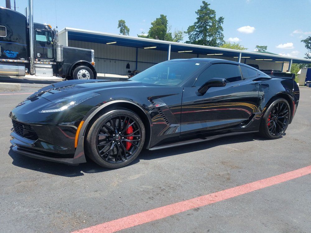A black corvette zr1 is parked in a parking lot next to a truck.