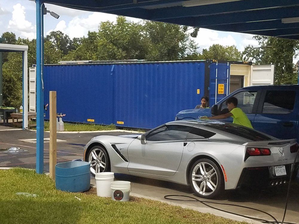 A silver sports car is being washed under a canopy