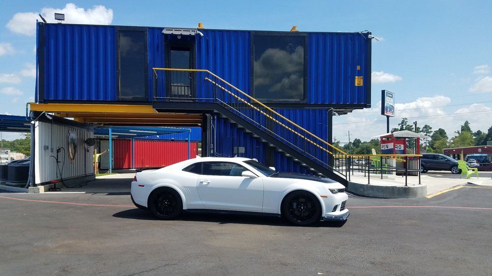 A white car is parked in front of a blue building with stairs leading up to it.