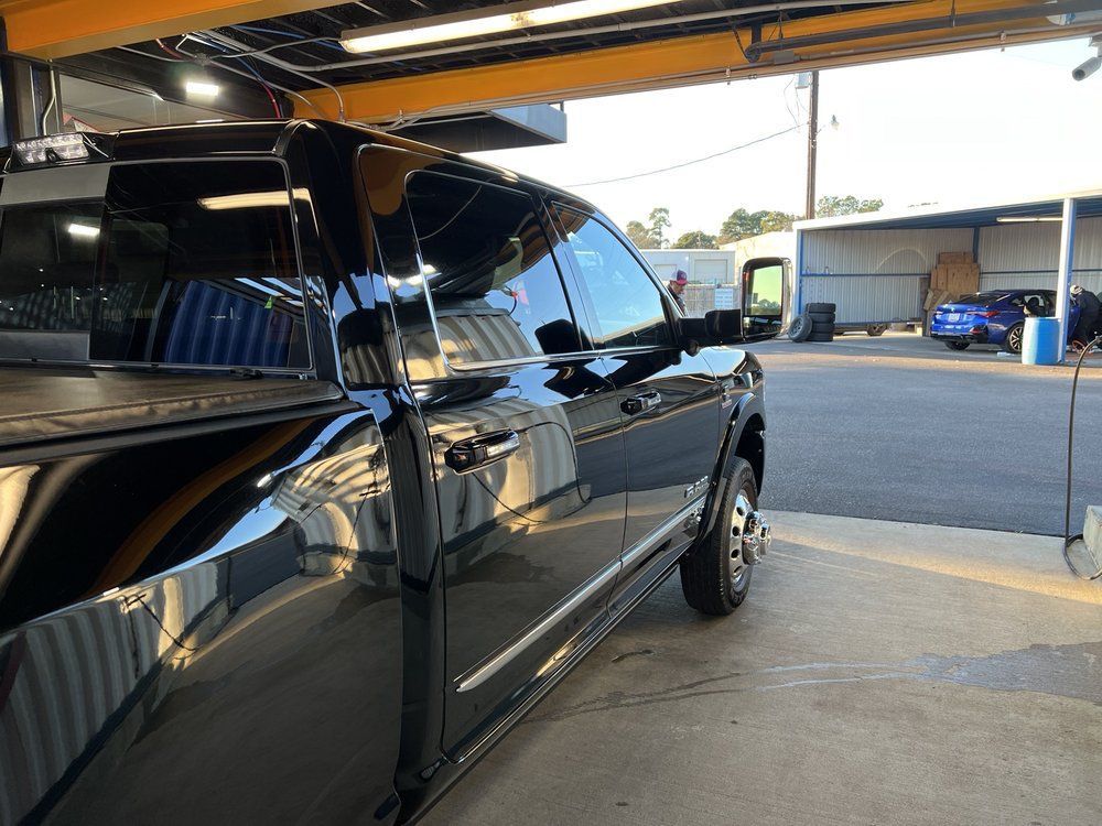 A black truck is parked in a parking lot under a crane.