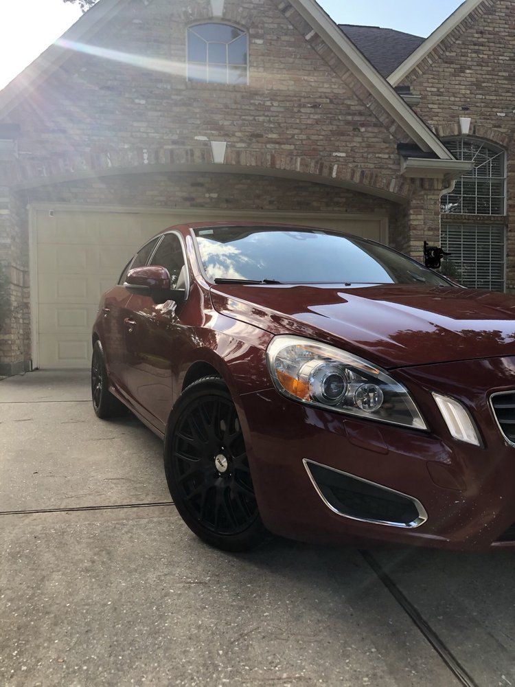 A red car is parked in front of a brick house.