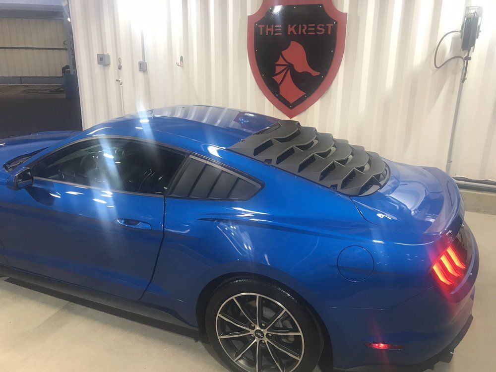 A blue mustang is parked in front of a sign that says the krist.