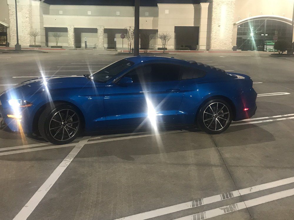 A blue mustang is parked in a parking lot at night.