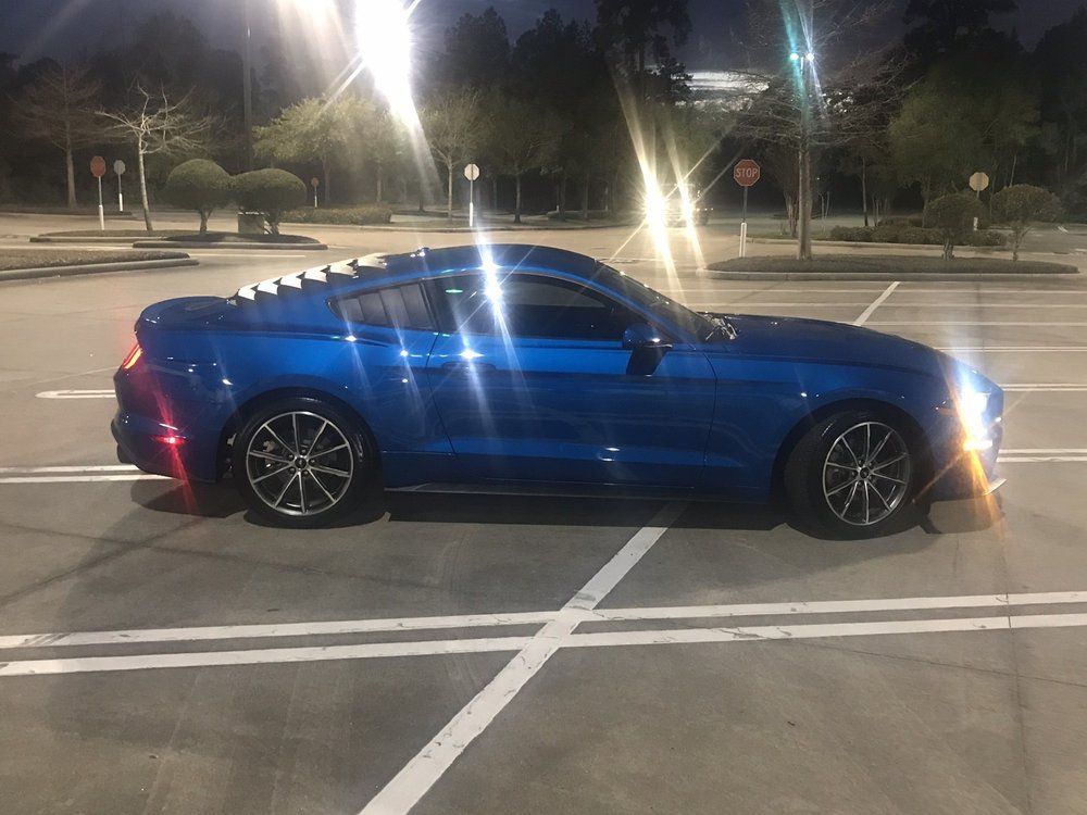 A blue mustang is parked in a parking lot at night.