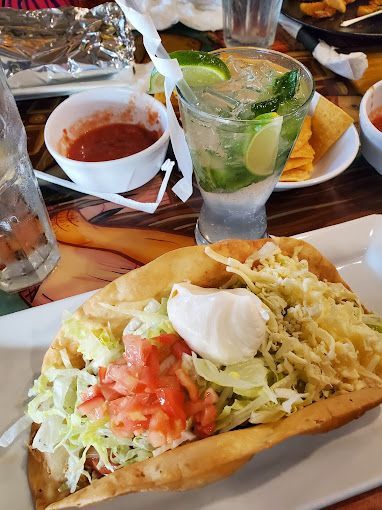 A taco is sitting on a white plate on a table next to a drink.