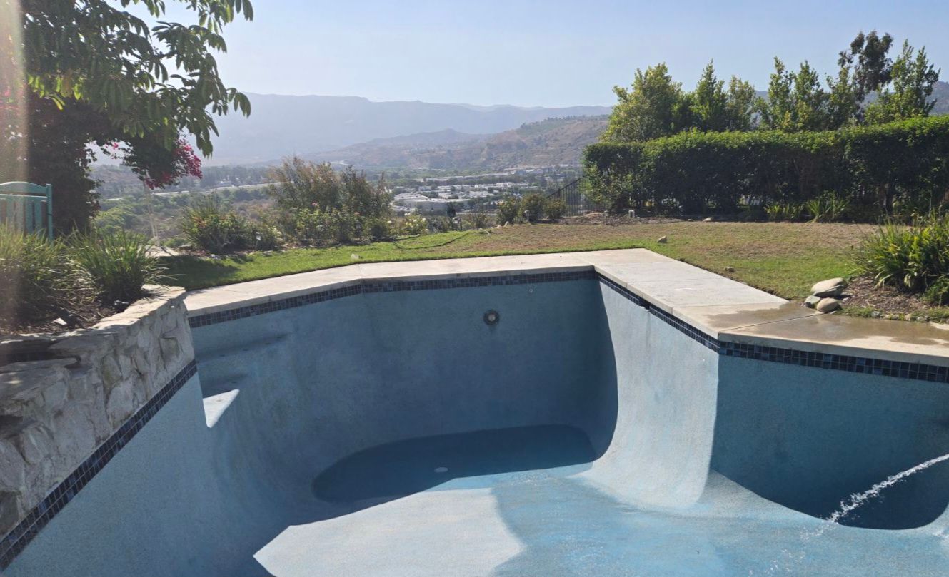 Empty swimming pool overlooking a scenic valley, with blue tile accents and a concrete deck.