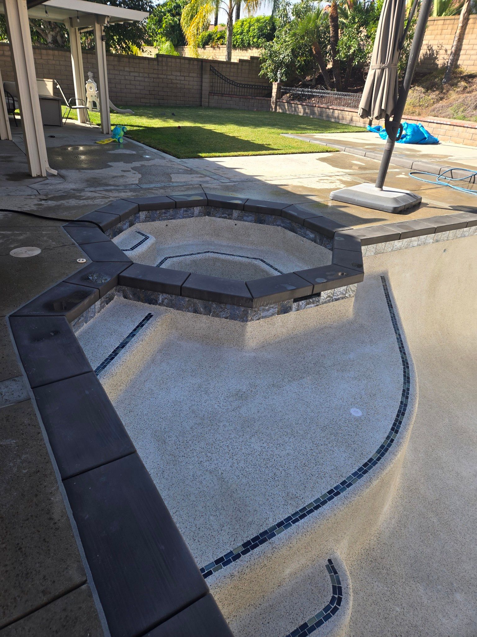 A backyard with a light-colored pool and a dark-bricked hot tub. The pool area features a dark-colored edge and steps.