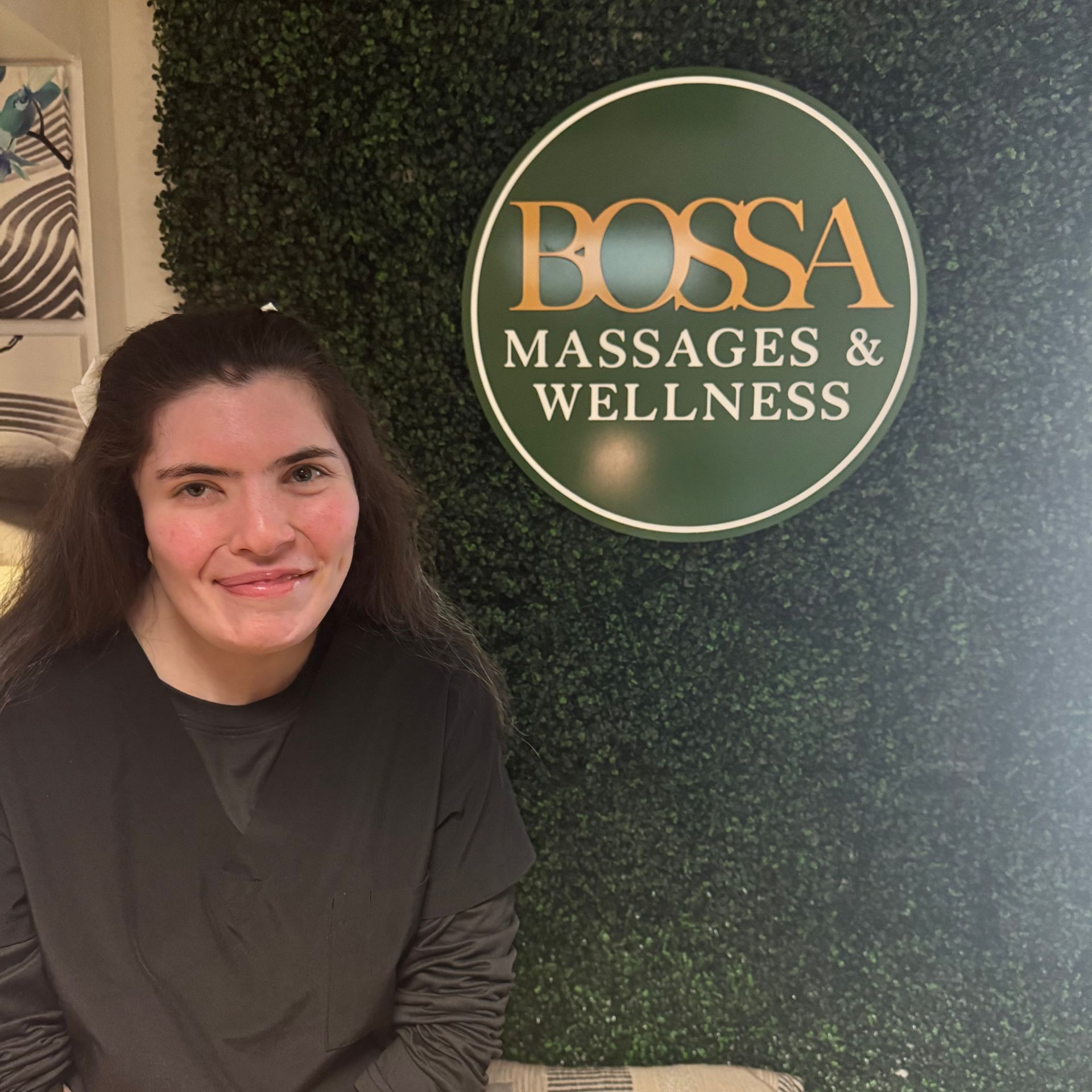 Smiling woman in light pink top against purple wall at Bossa Massages & Wellness