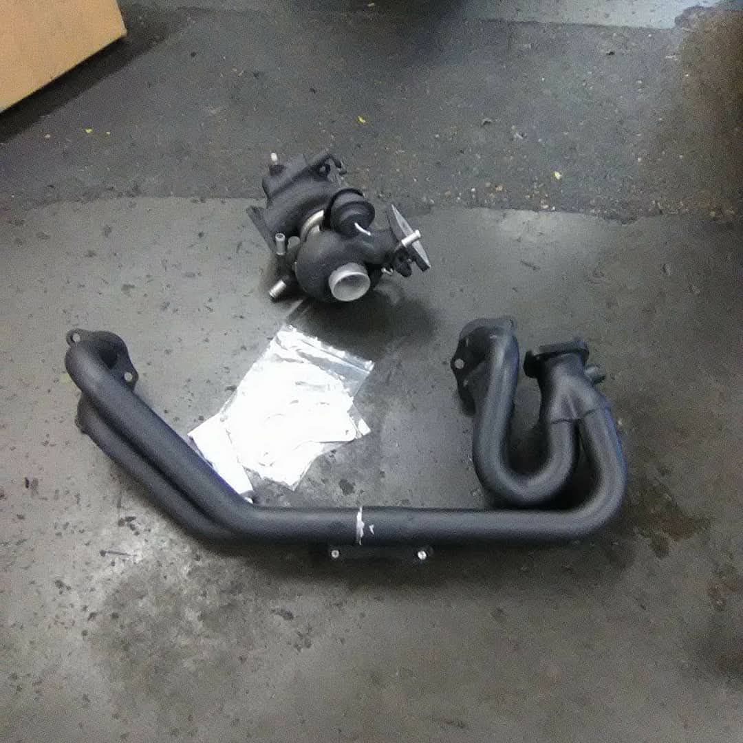Black turbocharger and exhaust manifold on a concrete floor.