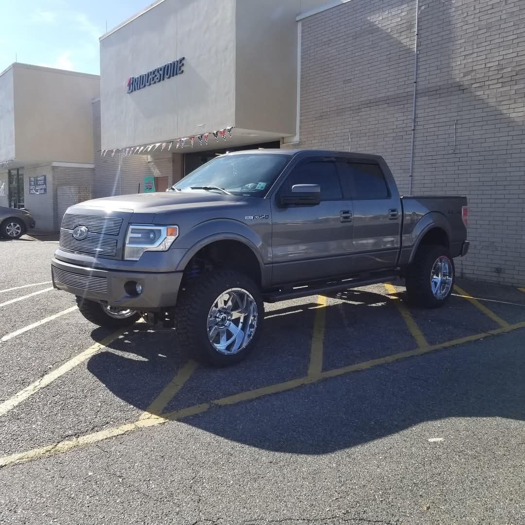 Gray pickup truck parked in front of a building with chrome wheels, lifted suspension, and tinted windows.