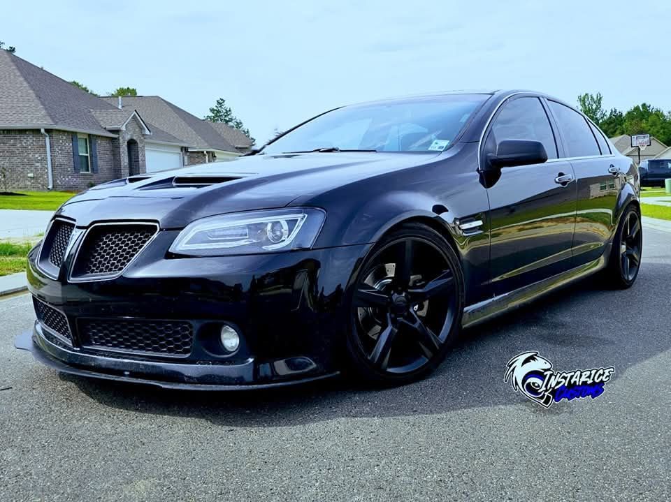 Black Pontiac G8 sedan with black rims parked on a street in front of houses on a sunny day.