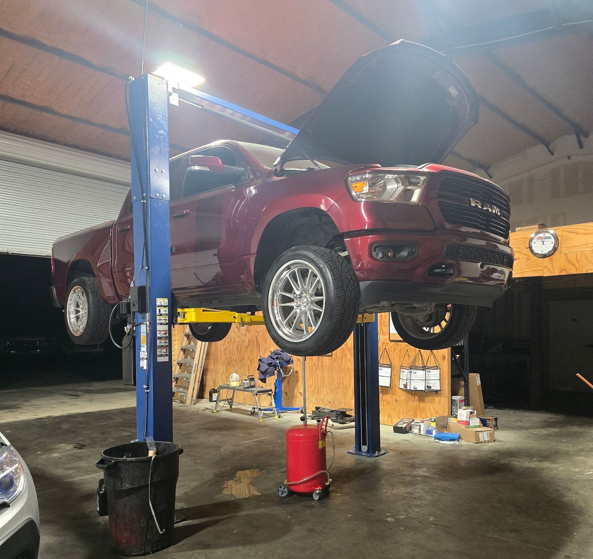 Red truck on a lift with hood open inside a garage.
