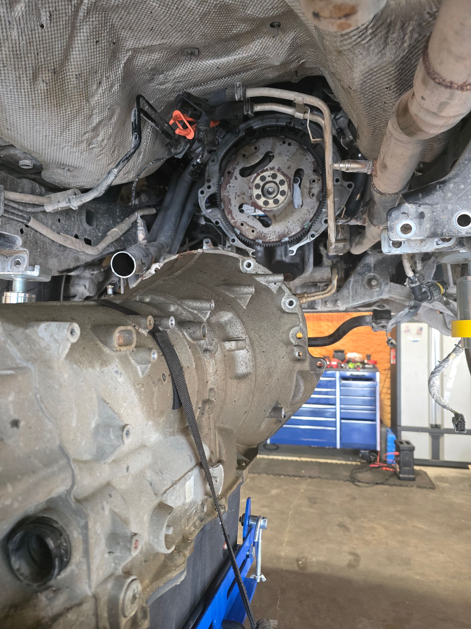 Car transmission being removed, showing engine components, garage setting.