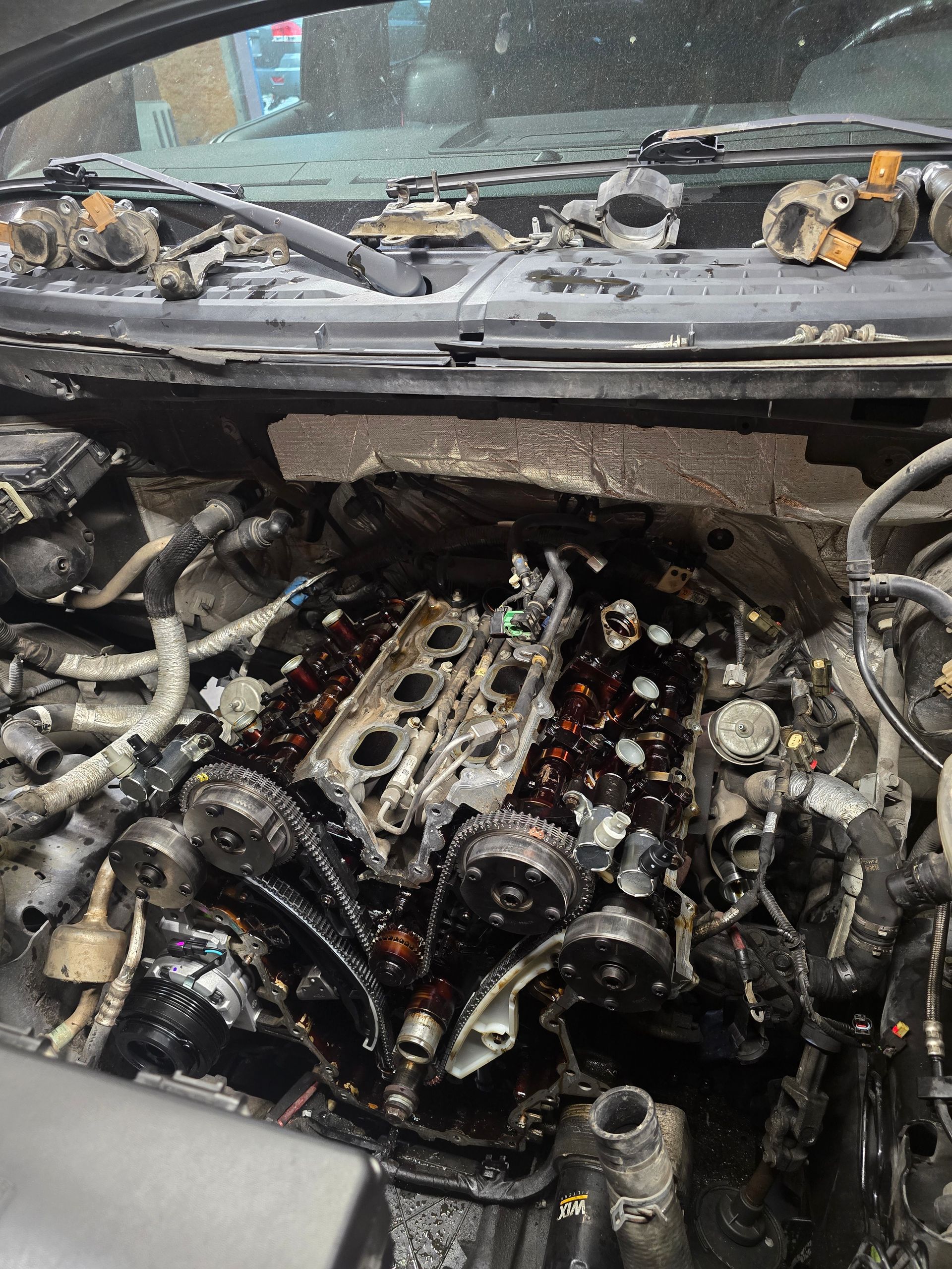 Engine covered in oil, visible spark plugs and other components; vehicle repair in progress.