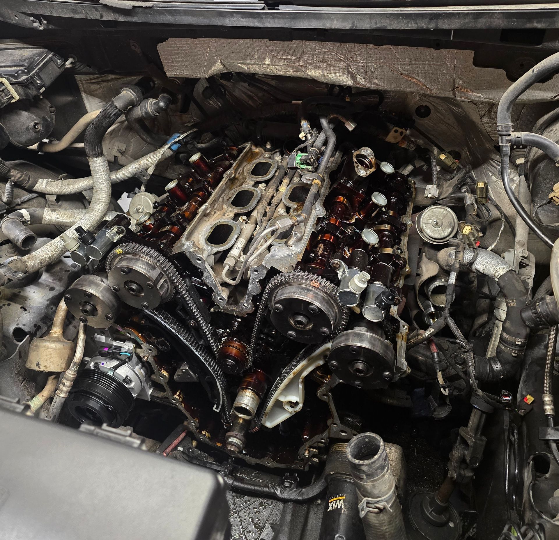 Car engine with removed valve covers, exposed components coated in oil.