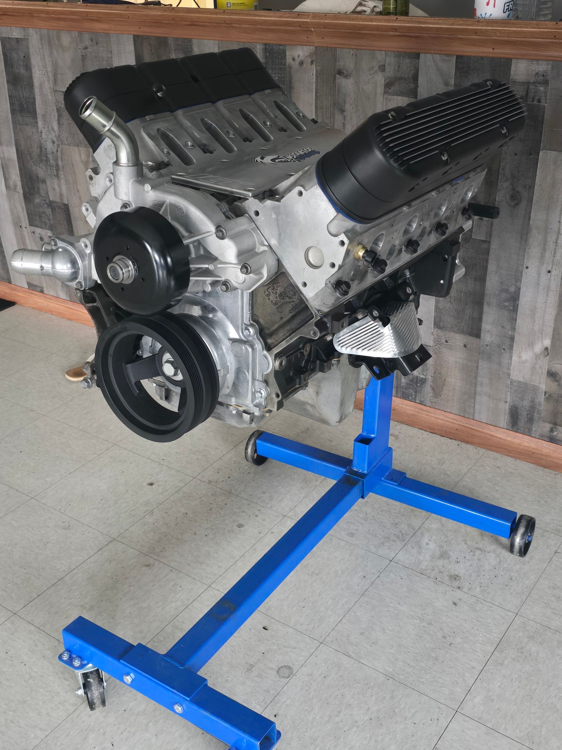 Blue engine stand holding a silver engine with black components, in a workshop.