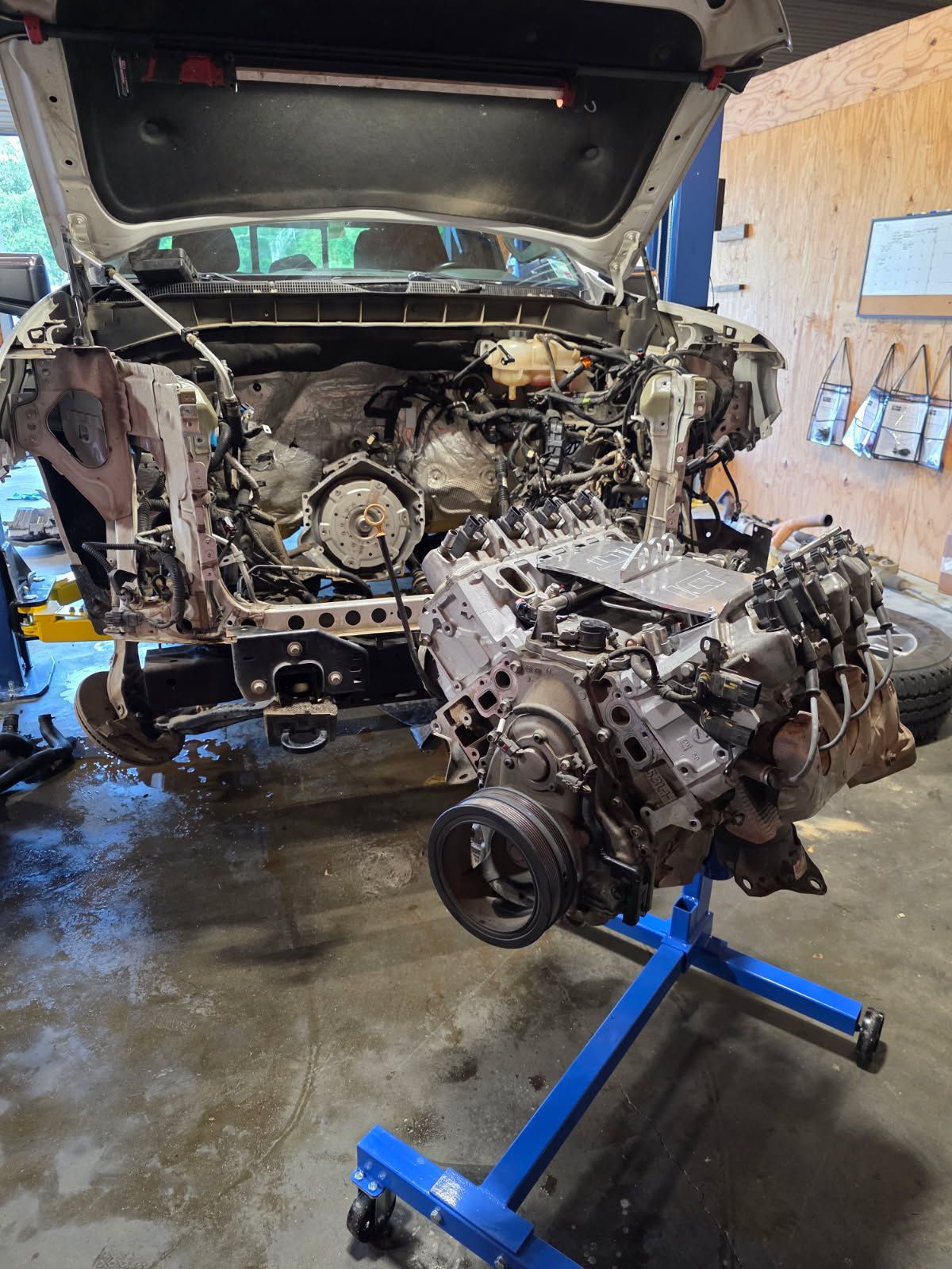 A gray suv with the hood up is parked in a garage.
