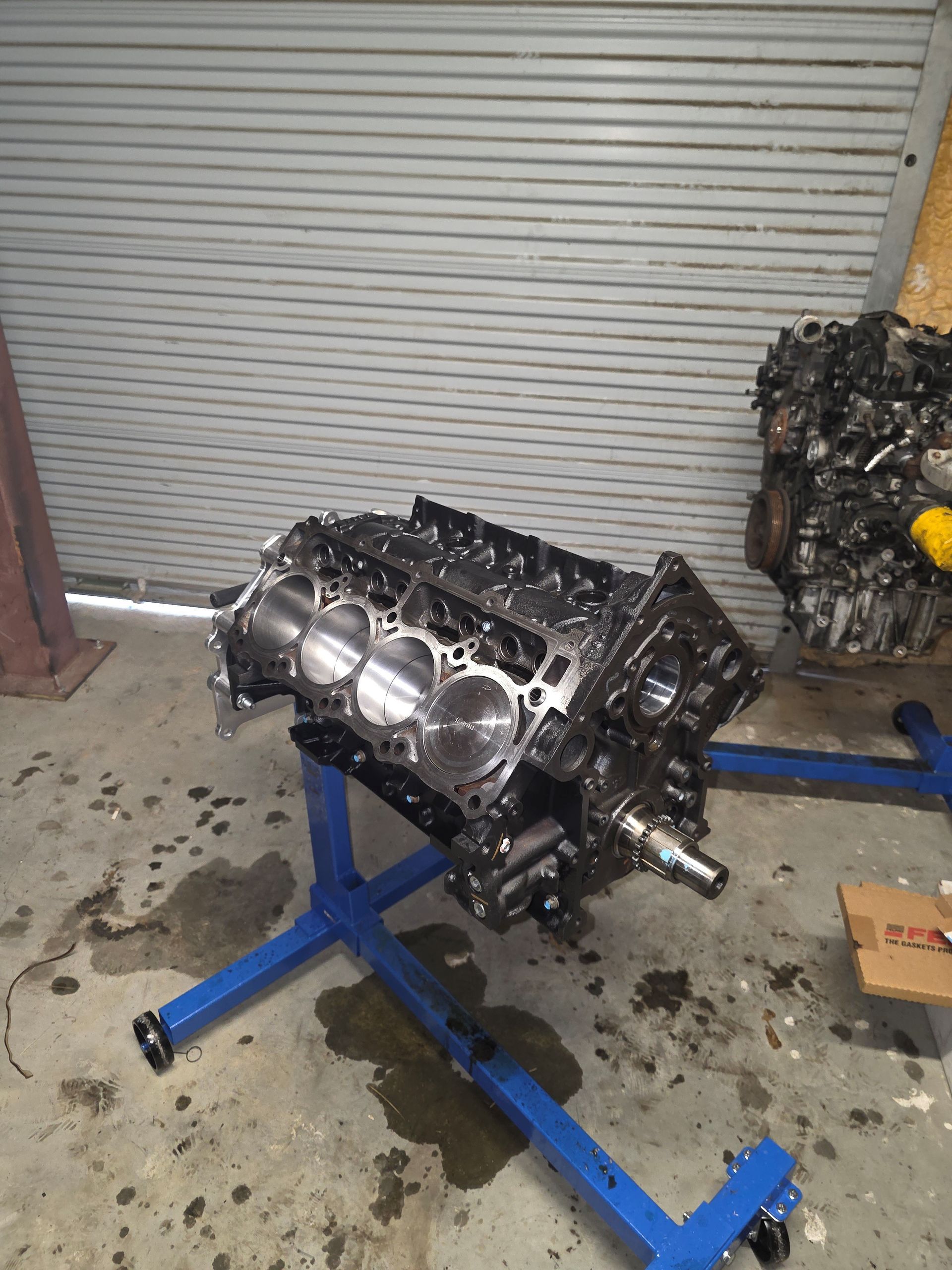 Engine block on a blue stand in a garage setting with a closed metal door in the background.