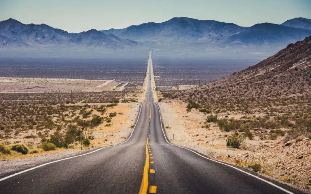 An empty highway in the desert with mountains in the background.